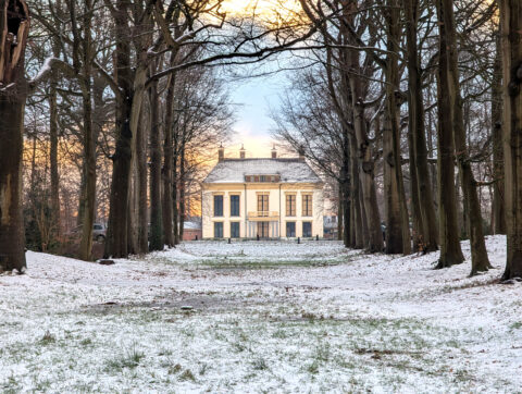 Landhuis te midden van besneeuwde bomen, omgeven door een winterse lucht.