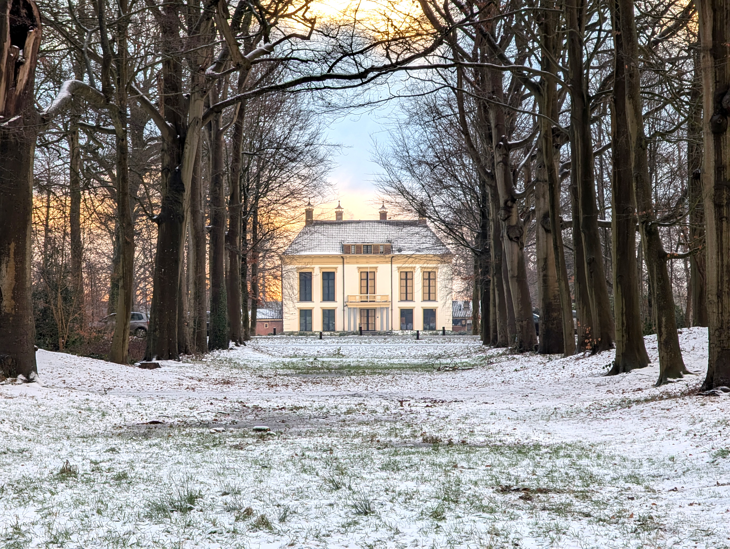 Landhuis te midden van besneeuwde bomen, omgeven door een winterse lucht.