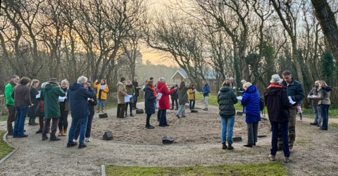 Een groep mensen staat in een kring buiten, omgeven door bomen bij zonsondergang.