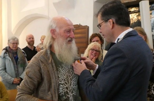 Een man krijgt een medaille opgespeld in een zaal met toeschouwers.
