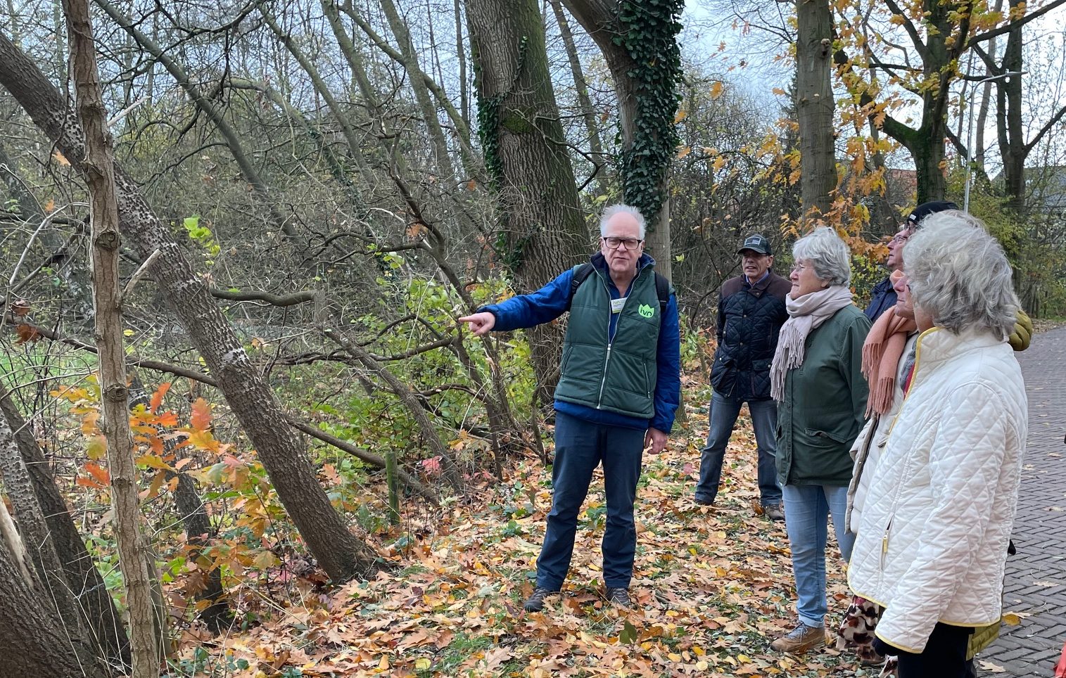 Een man geeft uitleg aan een groep mensen in een herfstig bos.