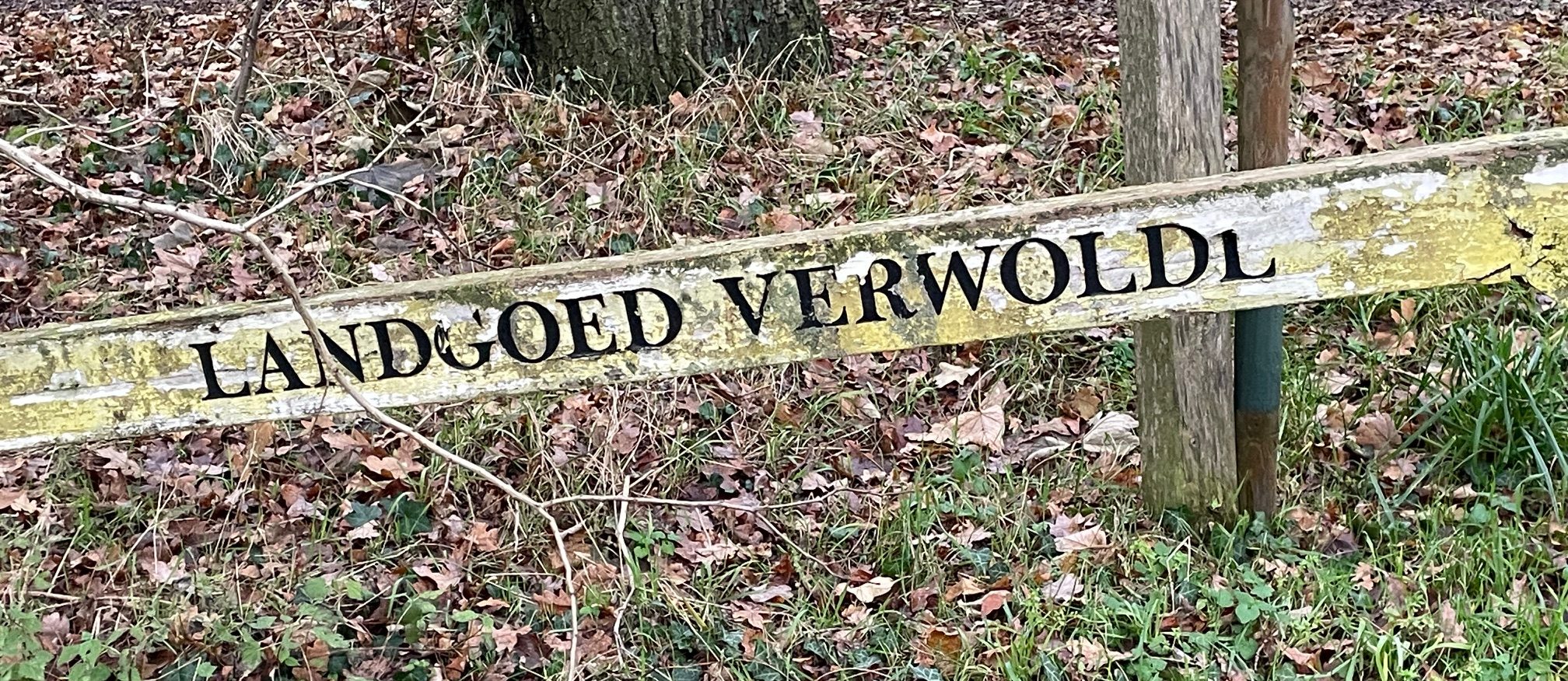 Vervallen bord met tekst "Landgoed Verwolde" in een bosrijke omgeving.