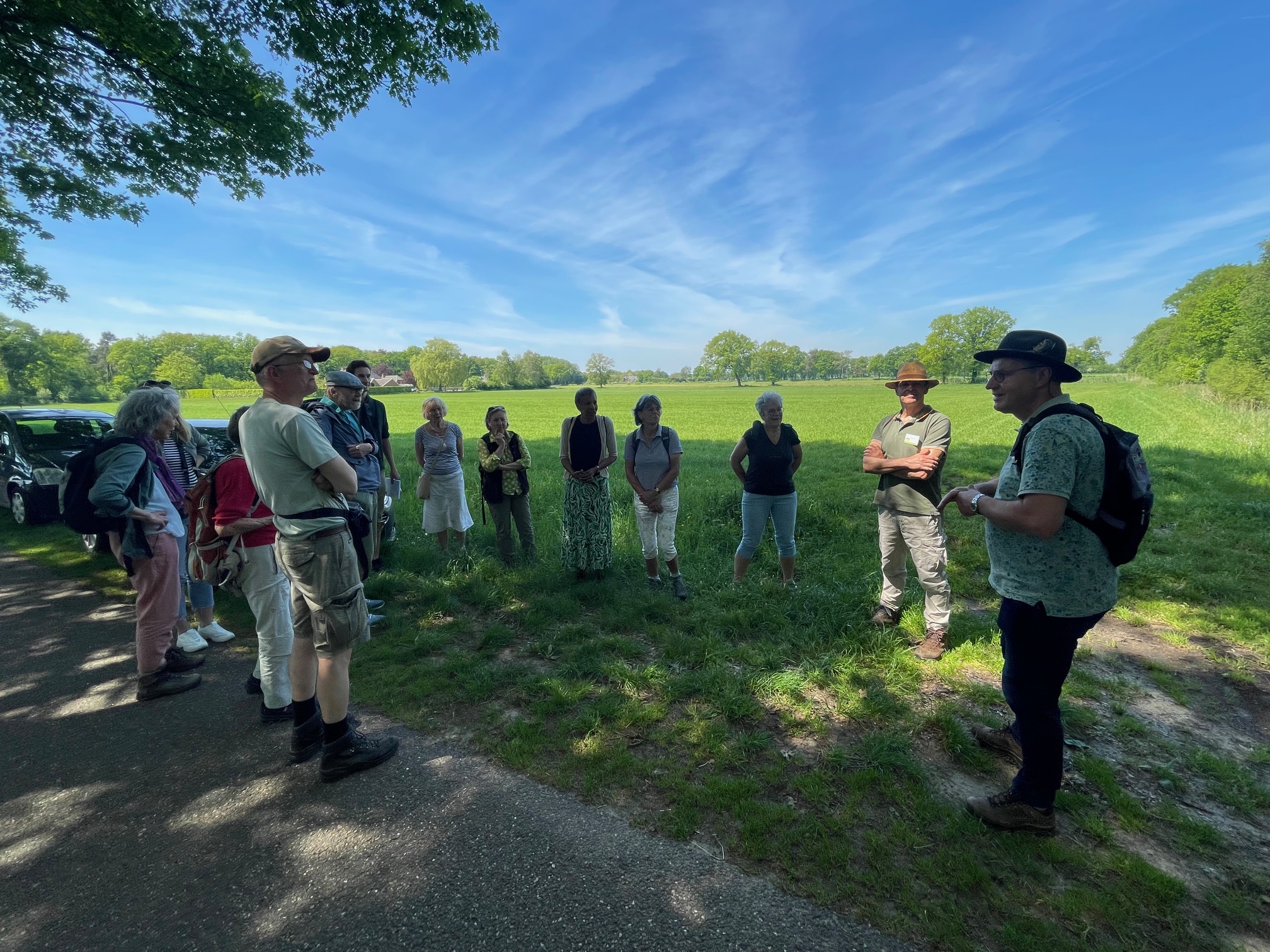 Een groep mensen staat in een kring op een grasveld tijdens een zonnige dag.