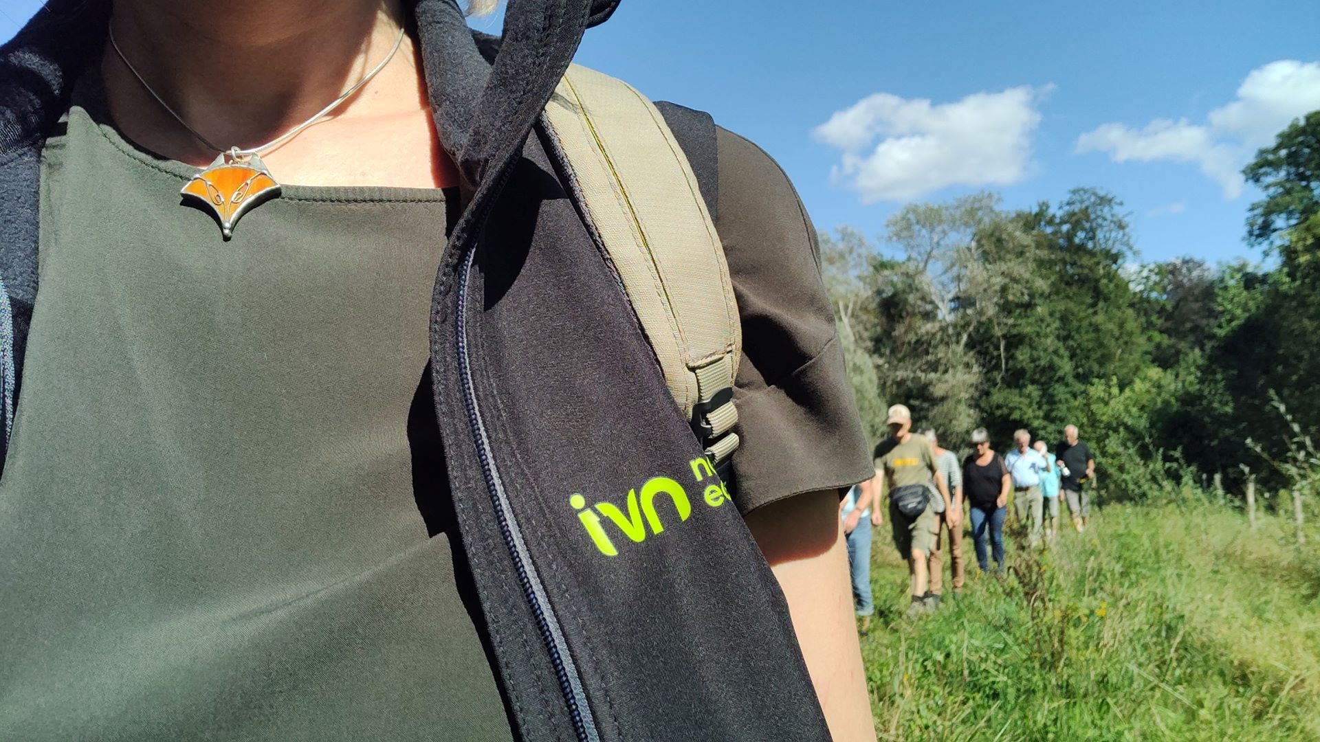 Een persoon met een IVN-vest leidt een groep mensen door een groene buitenomgeving.
