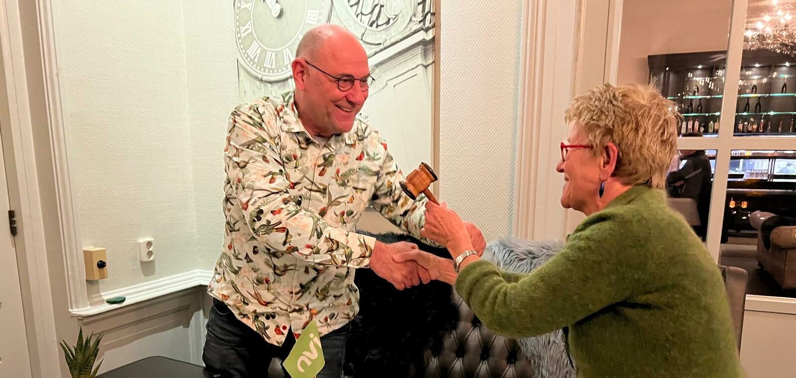 Twee mensen wisselen een houten hamer uit in een sfeervolle interieursetting.