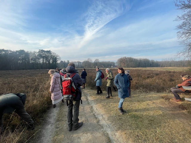 Groep mensen wandelt over een landelijke zandweg onder een bewolkte blauwe lucht.