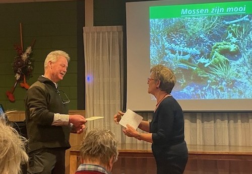 Man en vrouw praten voor een projectiescherm met de tekst "Mossen zijn mooi".