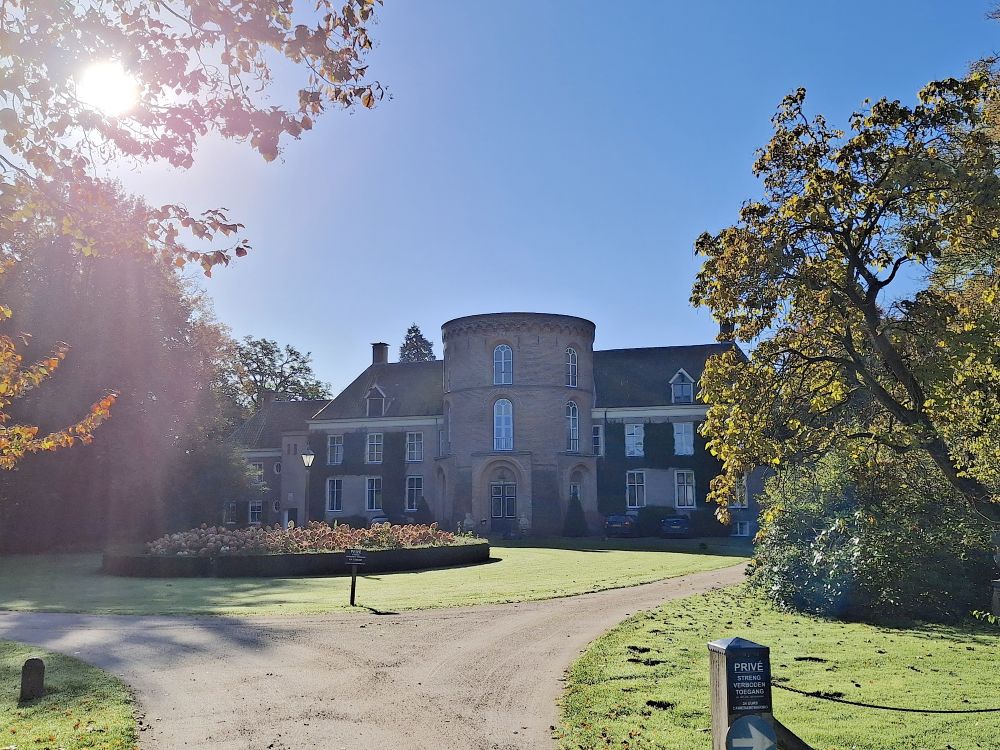 Kasteel met ronde toren, oprijlaan en herfstbomen onder een heldere blauwe lucht.