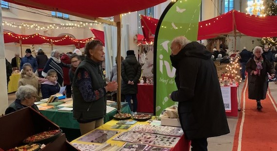 Kerstmarkt in een kerk met kraampjes en mensen die boeken en folders bekijken.