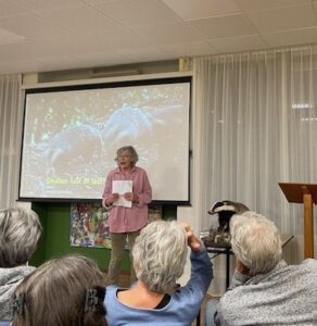 Persoon presenteert over dassen voor een klein publiek, met een dia op de achtergrond.