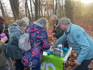 Mensen verzamelen zich rond een tafel in het bos voor een informele bijeenkomst met warme dranken.