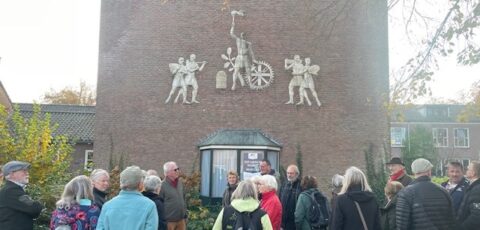 Groep mensen verzameld voor een bakstenen gebouw met reliëfkunst aan de muur.