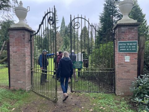 Een paar mensen loopt door een open hek in een park met bomen.