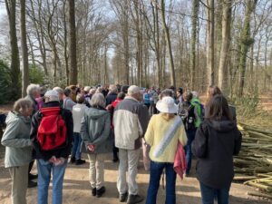 Groep mensen in een bos, bijeengekomen voor waarschijnlijk een rondleiding of bijeenkomst.