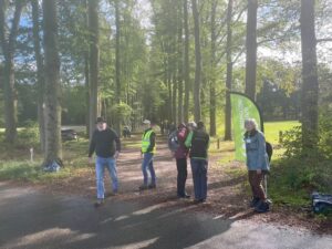 Groep mensen op bosweg, inclusief veiligheidshesjes. Groen vlaggetje aan de rechterkant.