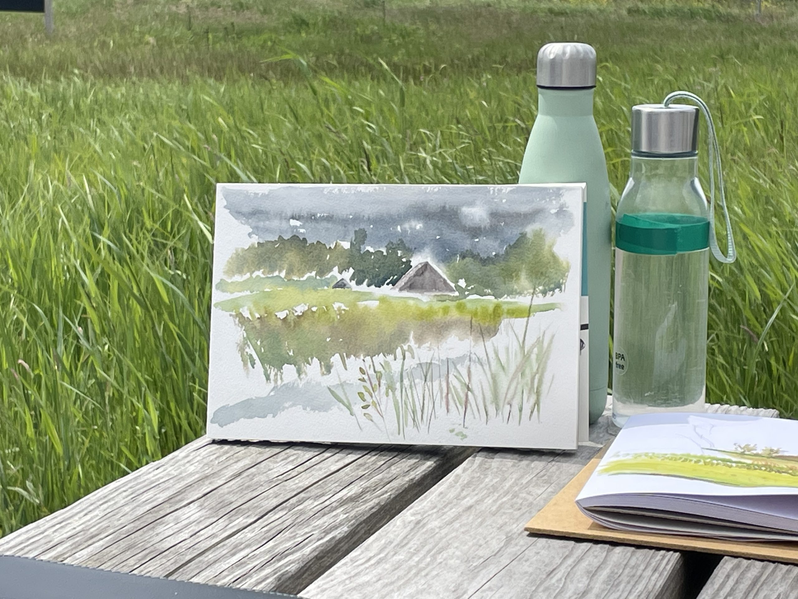 Schilderij van landschap op tafel met waterflessen en gras op achtergrond.