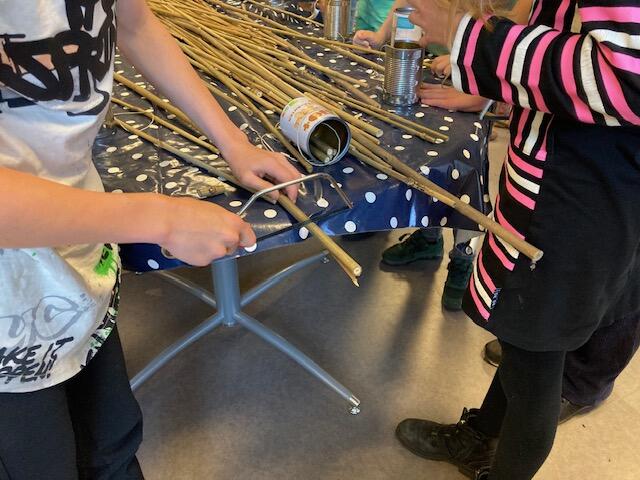 Kinderen zagen takken bij tafel met blikken; creatieve activiteit in binnenruimte.