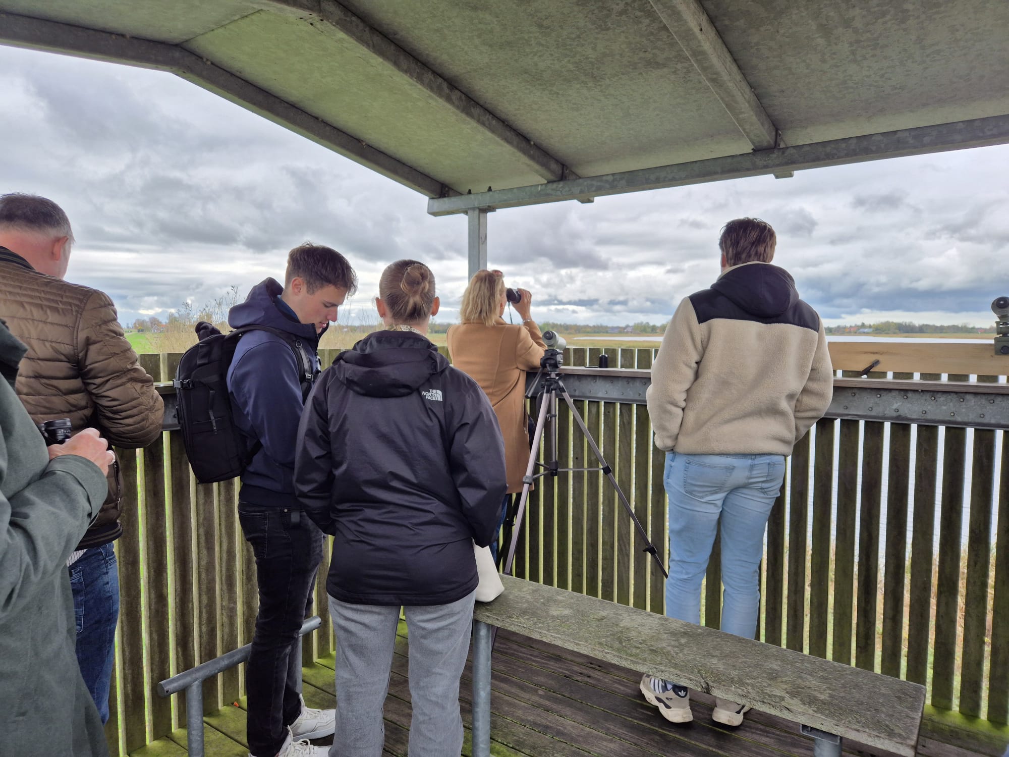 Mensen in een houten uitkijktoren observeren een natuurgebied met verrekijkers en camera's.