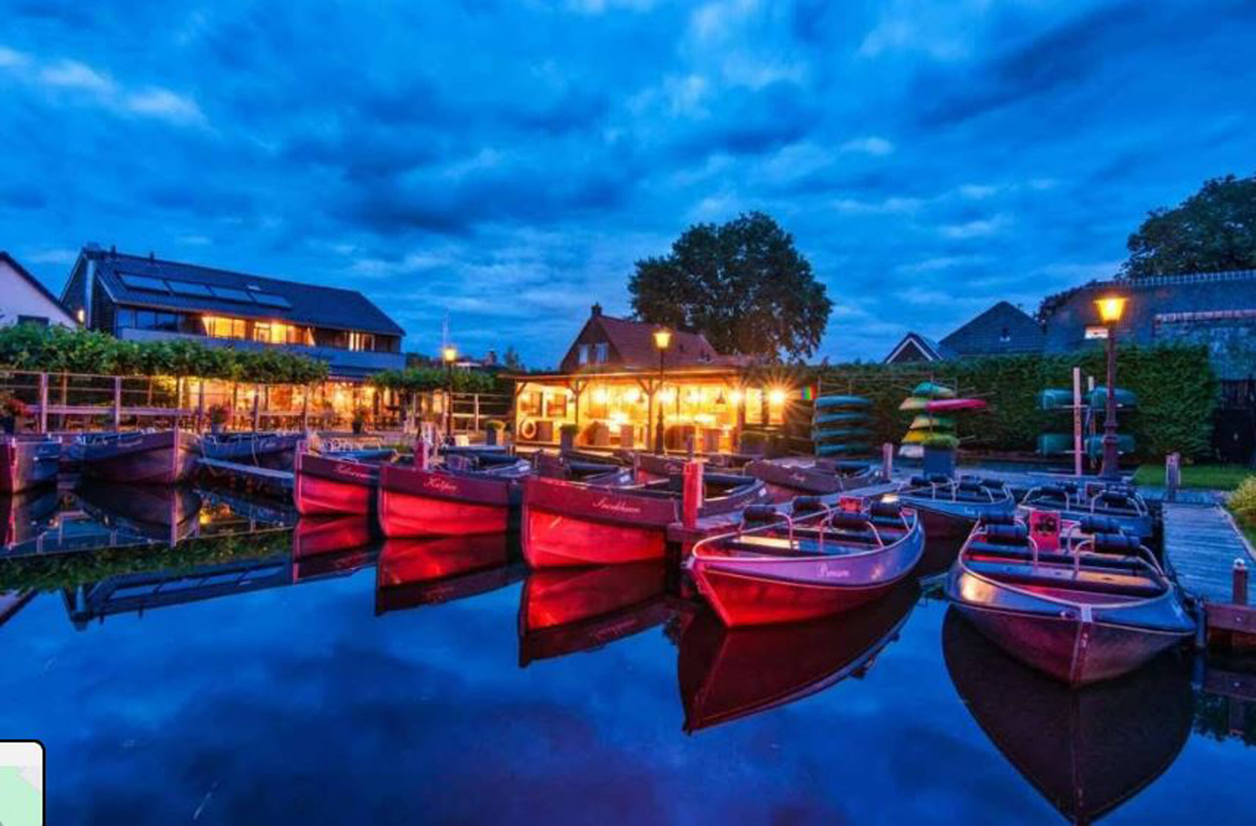 Rode boten aangemeerd bij een verlichte dok in de avondschemering met gebouwen op de achtergrond.