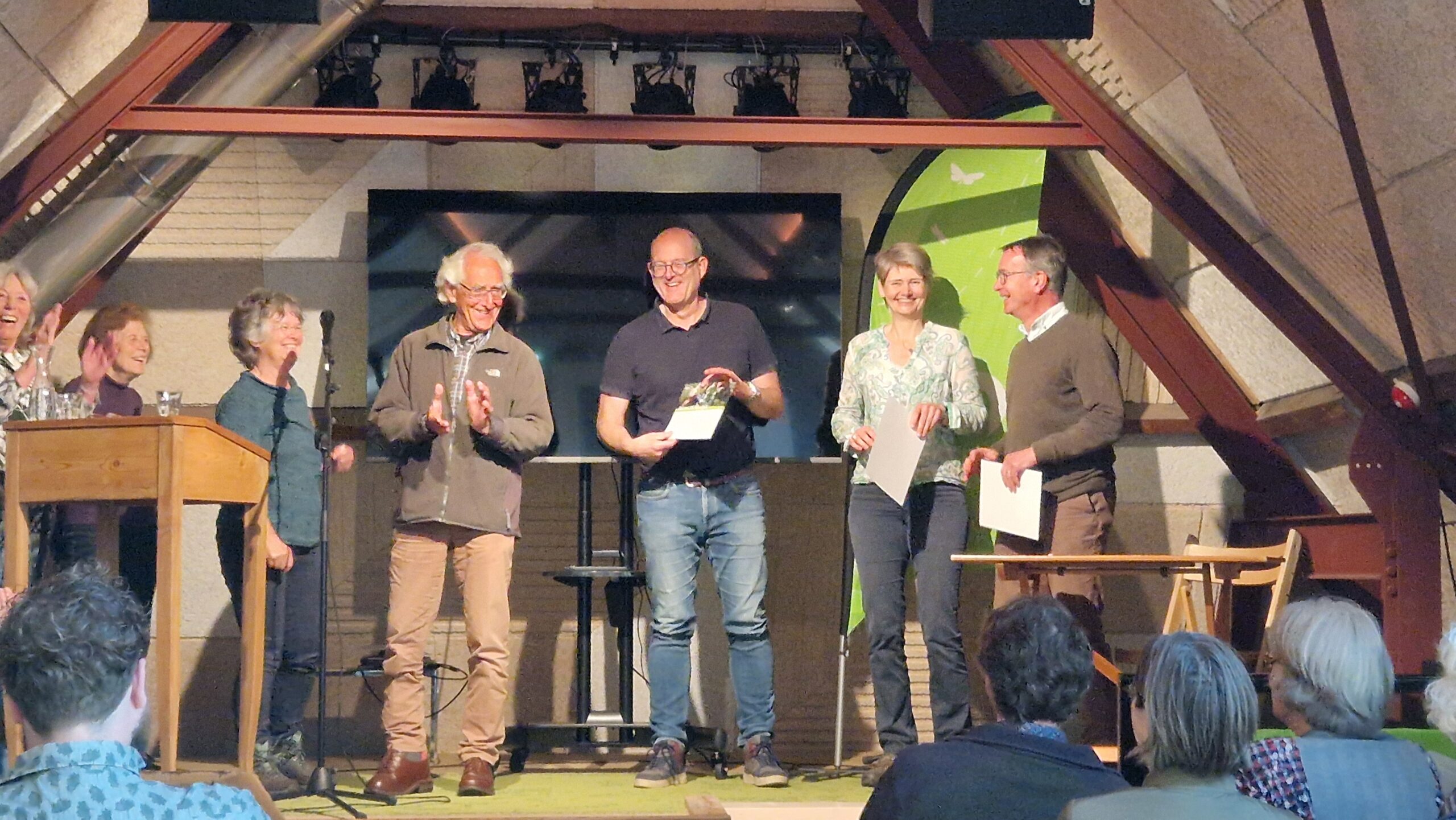 Een groep mensen viert op een podium; een man ontvangt een certificaat.