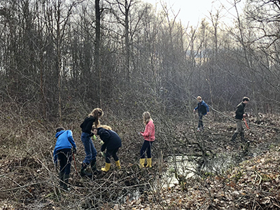Mensen werken in een bosrijk gebied, staan in modder, sommigen dragen gele laarzen.