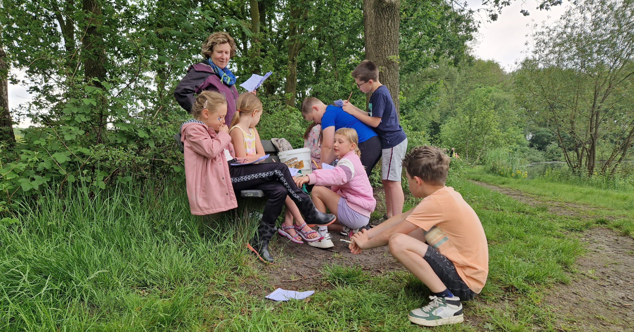 Groep kinderen en volwassene bezig met buitenactiviteiten in een bosrijke omgeving.