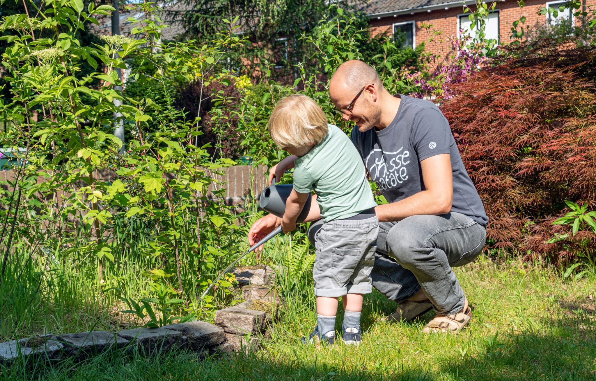 Vader en kind wateren samen planten in een groene tuin onder de zon.