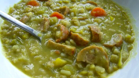 Bord met erwtensoep, met worst, wortel en stukjes groente, geserveerd met een lepel.