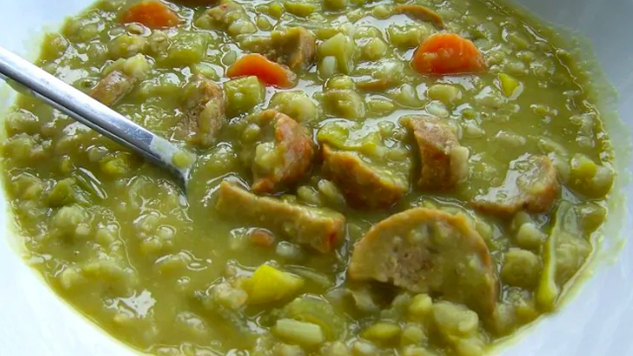 Bord met erwtensoep, met worst, wortel en stukjes groente, geserveerd met een lepel.