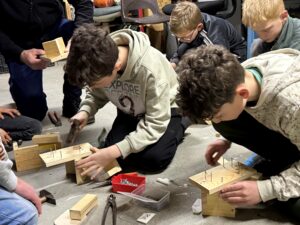 Kinderen timmeren samen houten constructies in een werkplaatsomgeving.