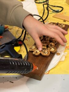 Een hand lijmt walnootschalen op hout met een lijmpistool.