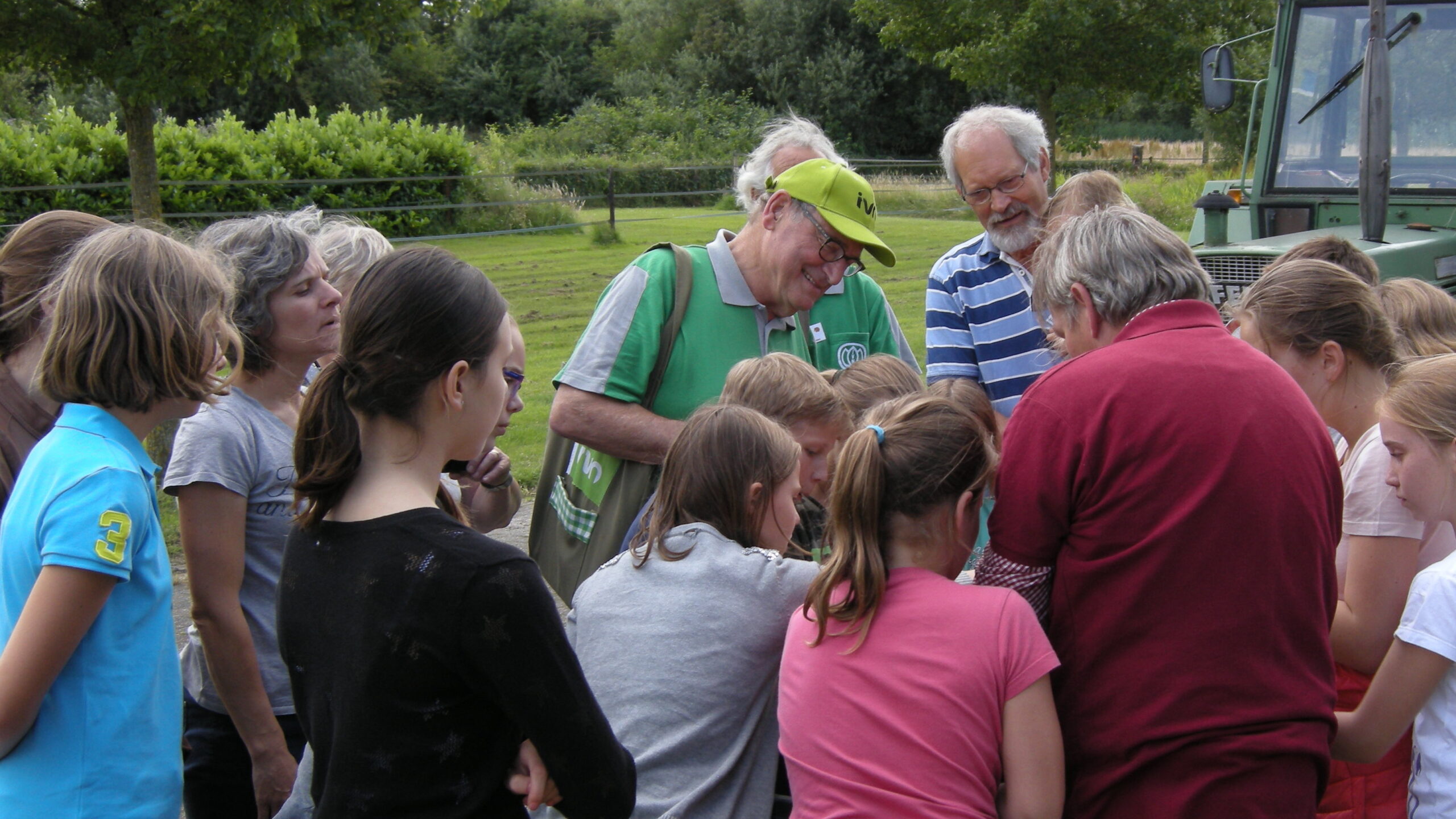 Groep mensen verzameld op een grasveld, met een man in groen die iets uitlegt.