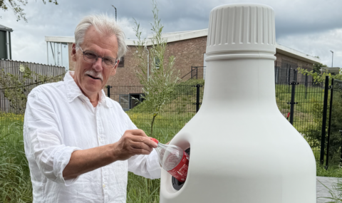 Man in wit overhemd deponeert fles in grote plastic container buiten.