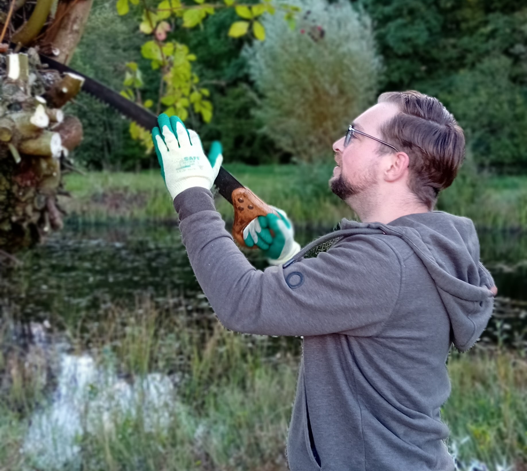 Man zaagt takken met een handzaag in een park, draagt handschoenen en hoodie.