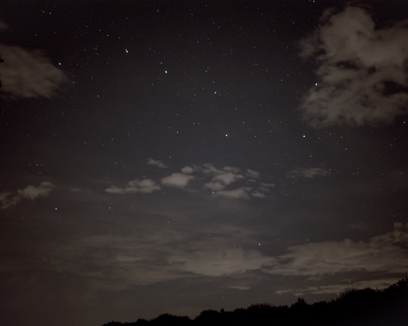 Sterrenhemel met verspreide wolken boven een donkere silhouet van een landschap.