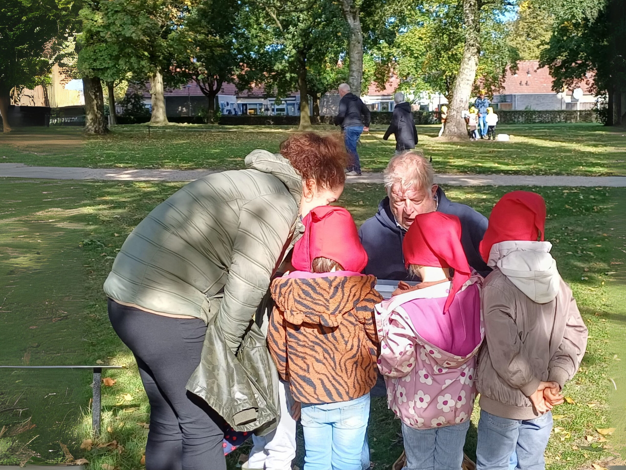Volwassenen en kinderen met rode hoeden bekijken iets in een park.