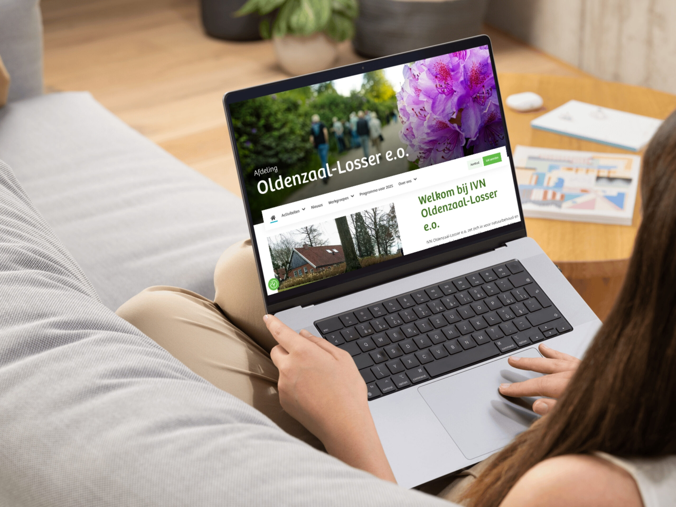 Vrouw bekijkt de website van IVN Oldenzaal-Losser op een laptop, zittend op een bank.