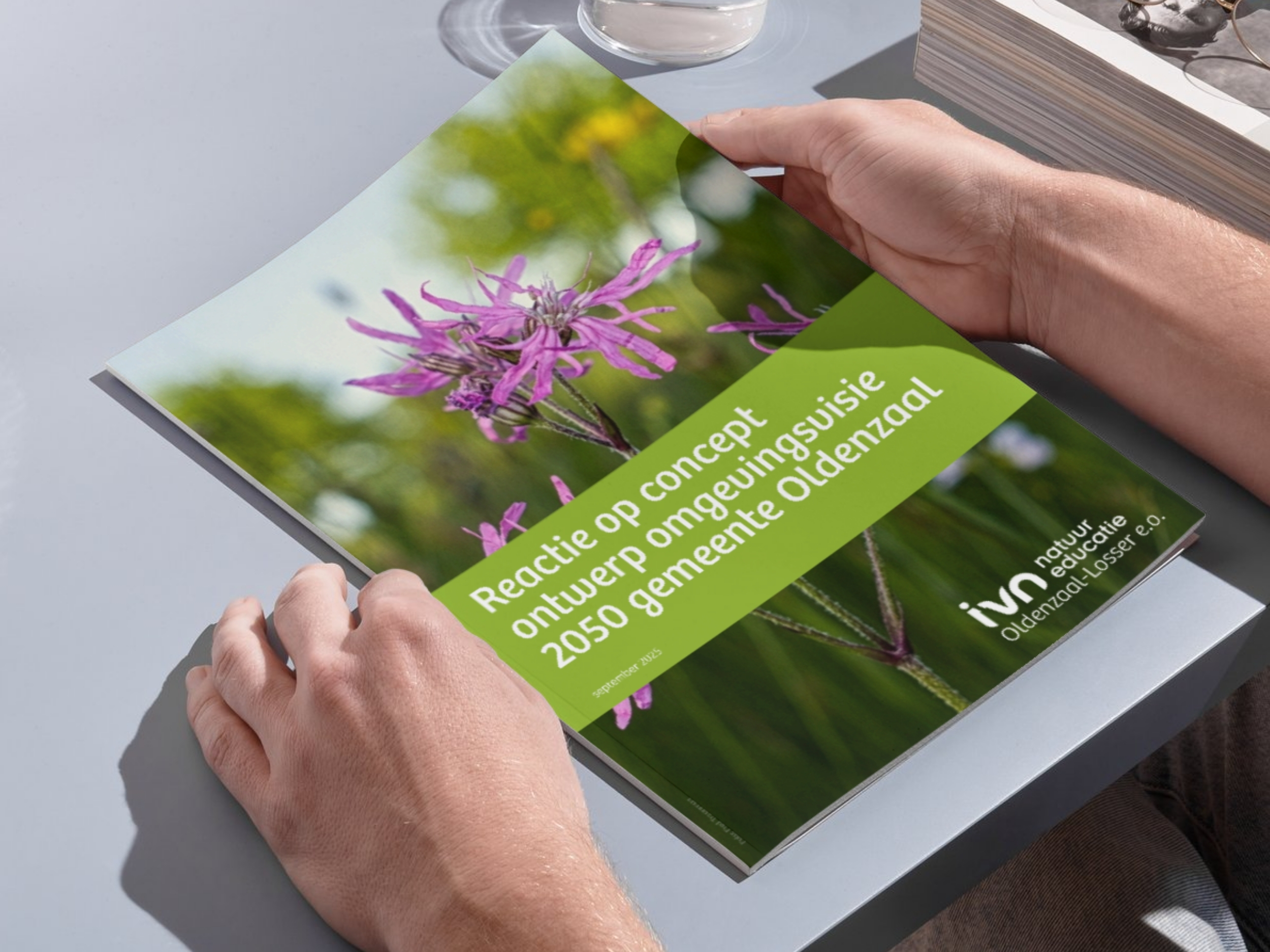 Twee handen houden een brochure vast met een foto van paarse bloemen en groene tekst.