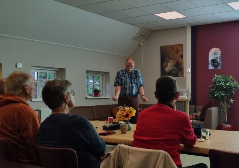 Man geeft presentatie aan een kleine groep mensen in een gezellige kamer met kunst aan de muur.