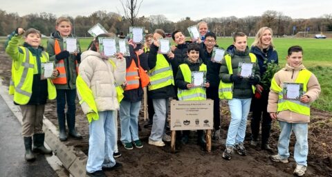 Groep kinderen in veiligheidshesjes toont boomcertificaten op Boomfeestdag.