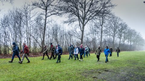 Groep mensen wandelt in de natuur op een mistige dag, omringd door kale bomen.