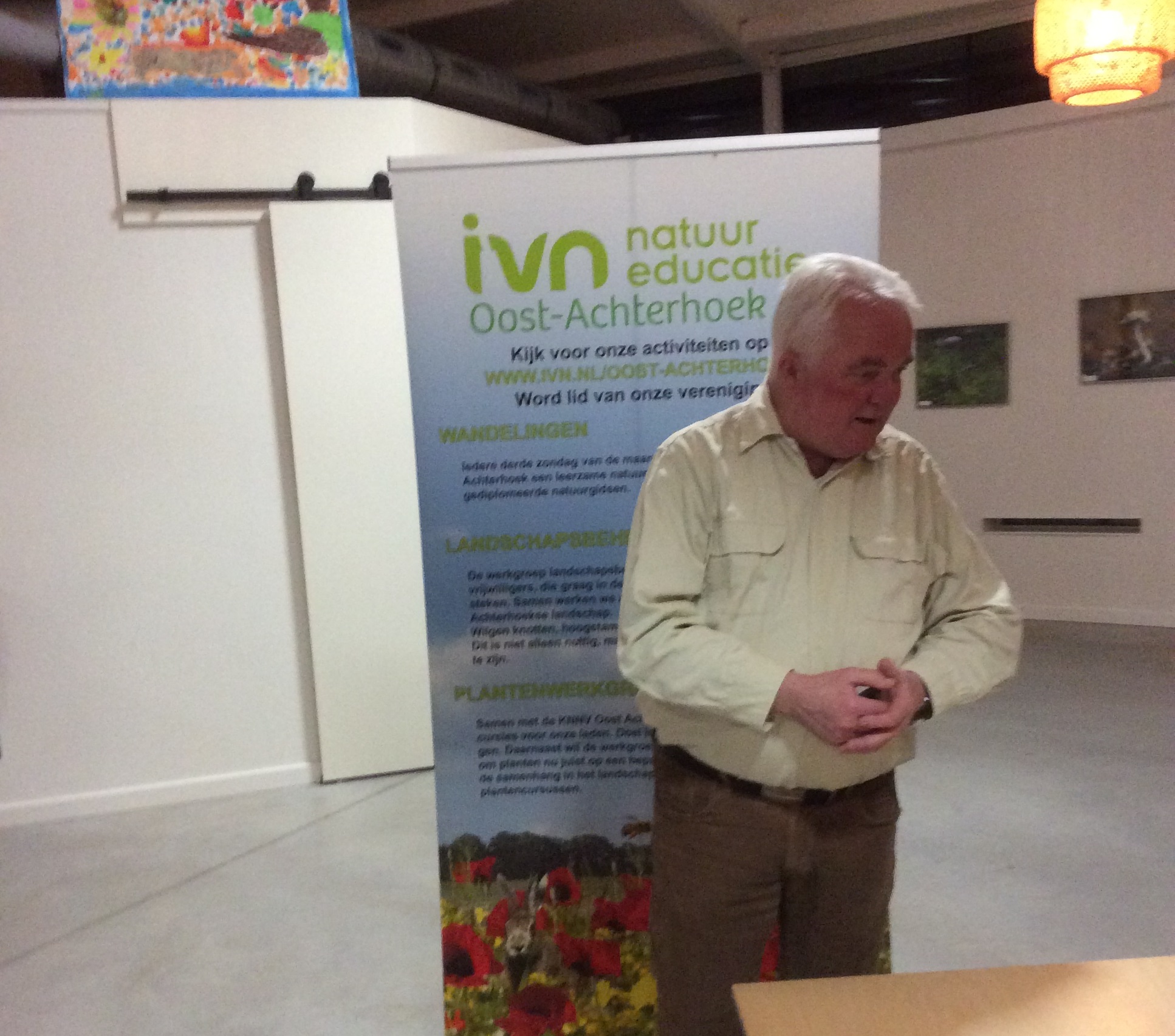 Een man staat voor een banner van IVN Oost-Achterhoek in een expositieruimte.