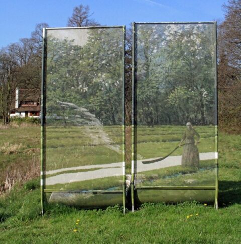 Transparant scherm in een veld met een schilderij van een landschap en een vrouw met een sikkel.