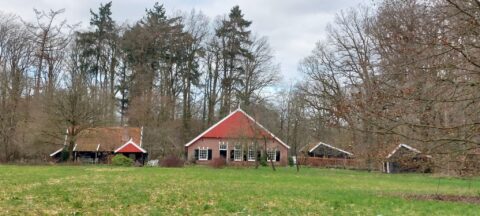 Rood bakstenen boerderij omringd door bomen, met een grasveld op de voorgrond.