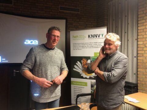 Twee mannen voor een projectiescherm en banner van IVN en KNNV in een vergaderruimte.