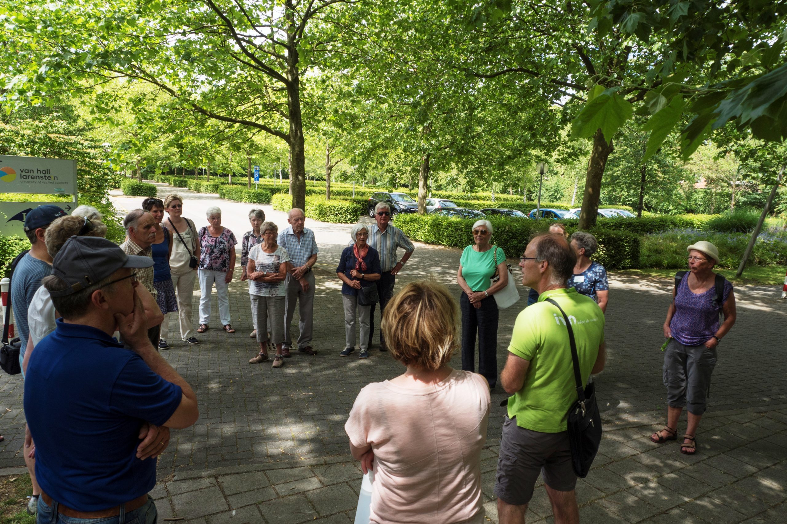 Groep mensen staat in een cirkel onder groene bomen buiten.