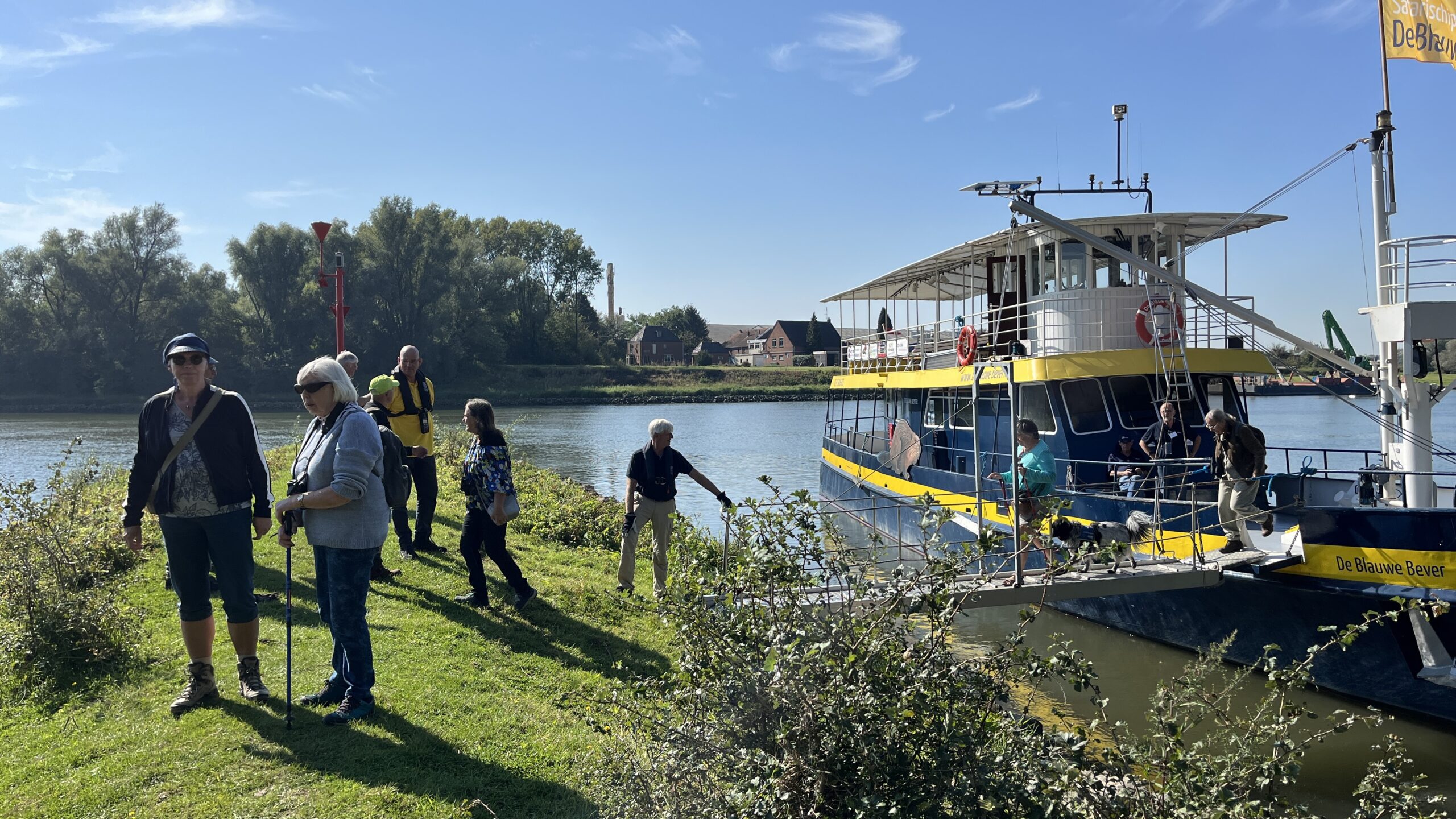 Mensen stappen van een geel-blauwe boot aan wal bij een rustige rivier.