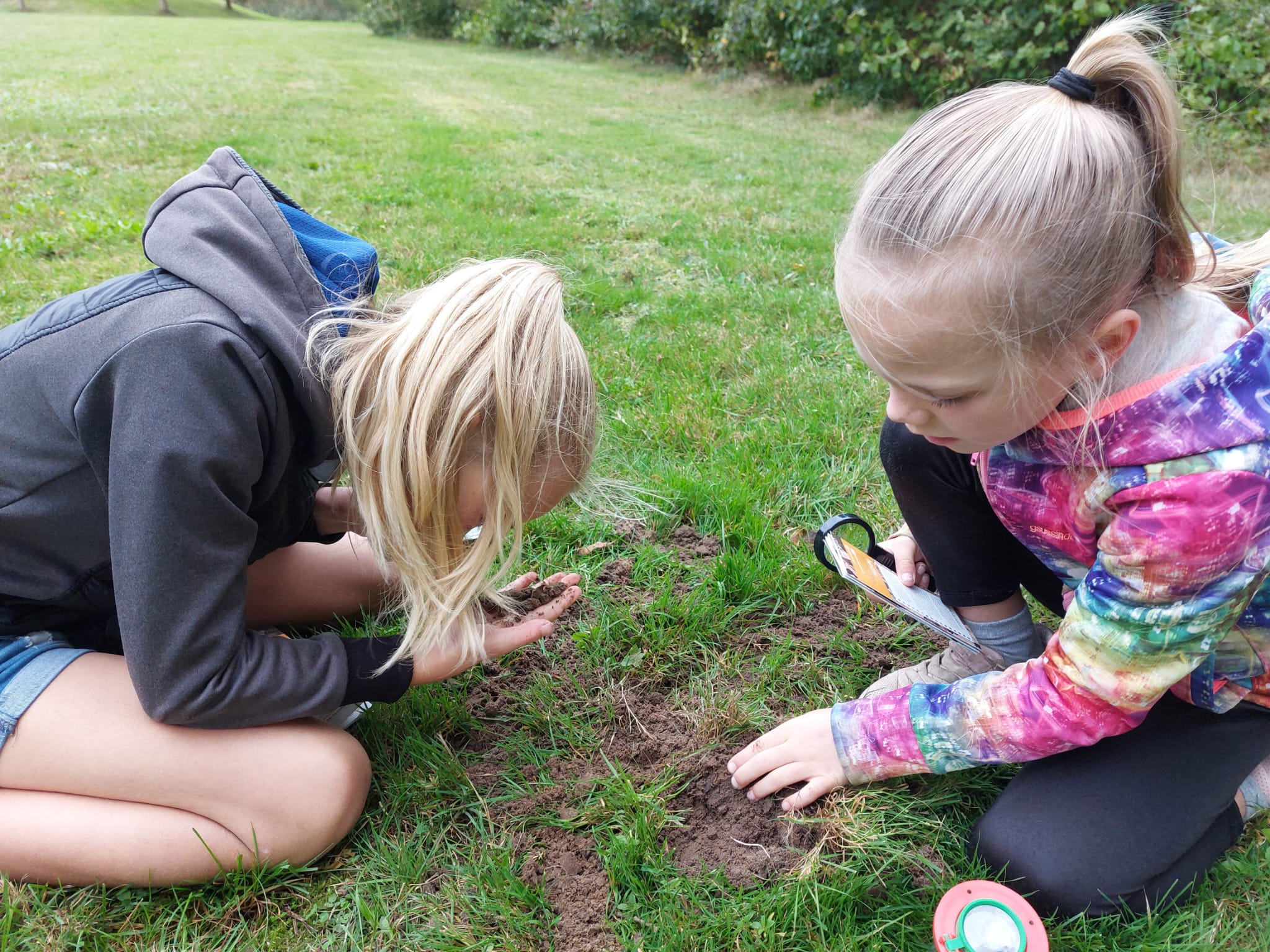 Twee kinderen onderzoeken de grond in een grasveld met een vergrootglas.