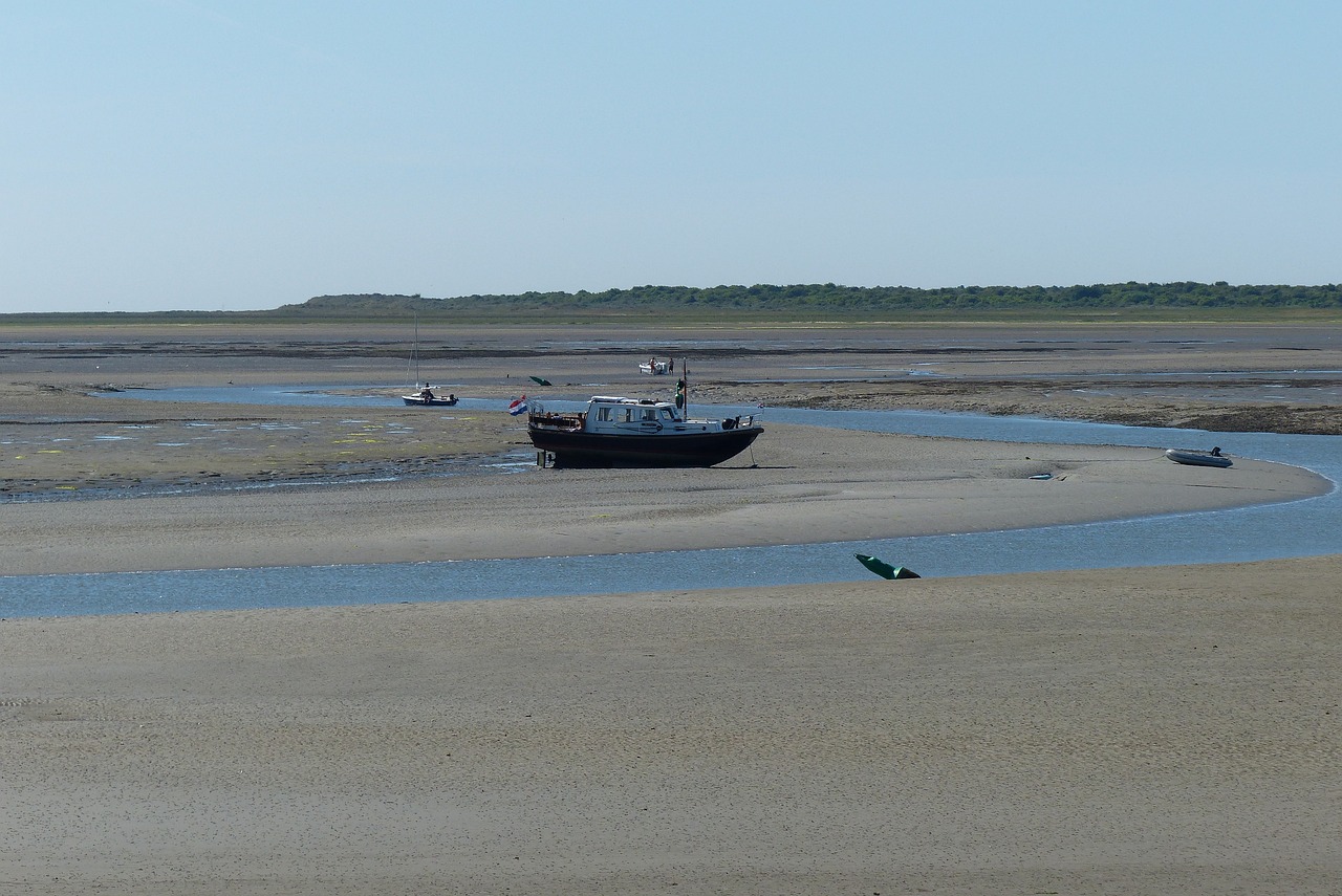 Boot op drooggevallen zandbank bij eb, omgeven door smalle watergeul en uitgestrekt landschap.