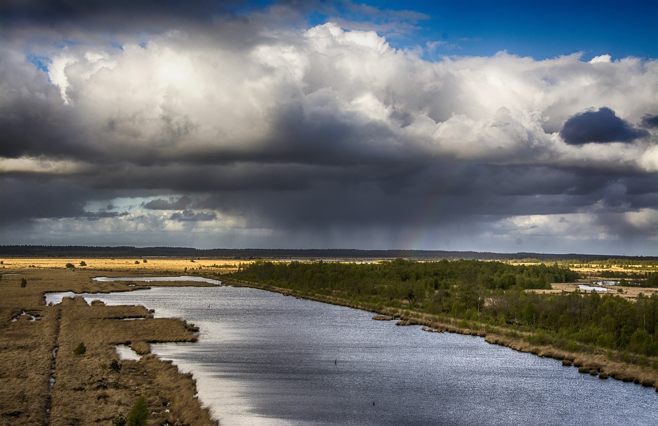 Brede rivier in landschap met donkere regenwolken en opklaringen in de verte.